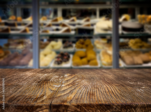 An empty wooden table against the background of a display case with sweets. Cafe, restaurant, coffee shop. Background. The backdrop. Evening. Night. Interior. Confectionery. Sweets. Copy space