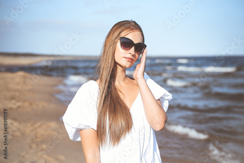 Happy smiling blonde woman is posing on the ocean beach with sunglasses