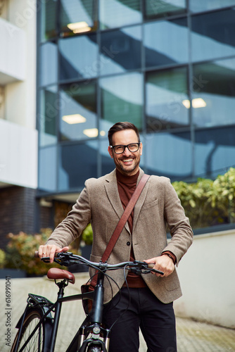 A smiling businessman with a briefcase walking on foot with a bicycle.