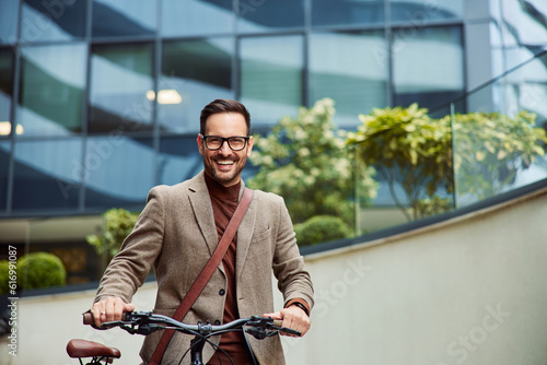 Portrait of a happy businessman pushing a bicycle in front of the company.