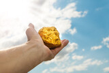 Gold nugget in a man's hand raised to the sky. The concept of wealth and success in the financial sector. Treasure, investment. Mining industry.