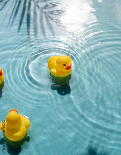 Bright yellow rubber ducks float in blue water pool. Hot summer resort vacation concept