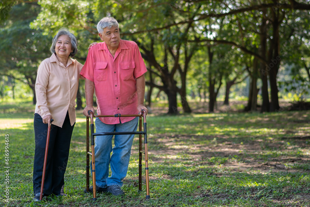 An old elderly Asian man uses a walker and walks in the park with his wife. Concept of happy retirement With Love and care from family and caregiver, Savings, and senior health insurance An old elderly Asian man uses a walker and walks in the park with his wife. Concept of happy retirement With Love and care from family and caregiver, Savings, and senior health insurance