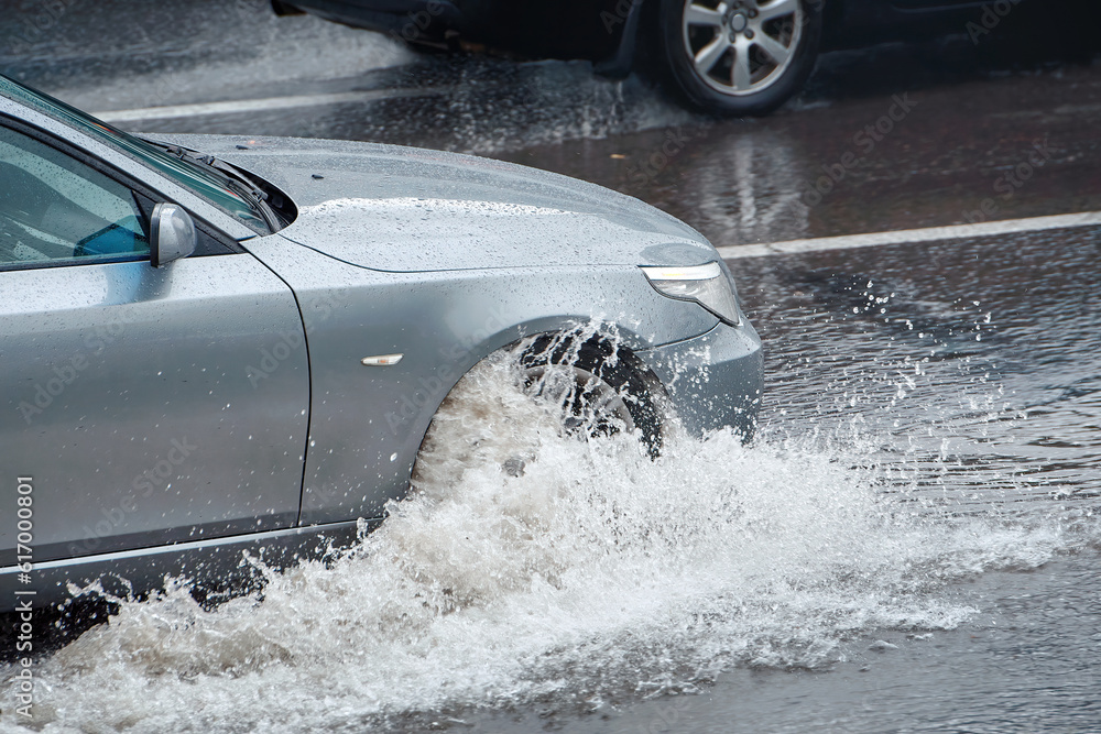 Car driving through puddle during heavy rain, mooving fast on wet road
