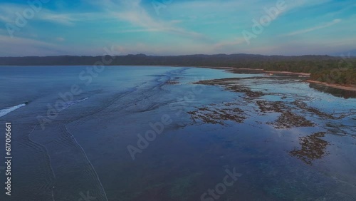 Drone shot at sunset across the shoreline of Grajagan bay on the island of Java in Indonesia, showing healthy coral reef and calm ocean waters photo