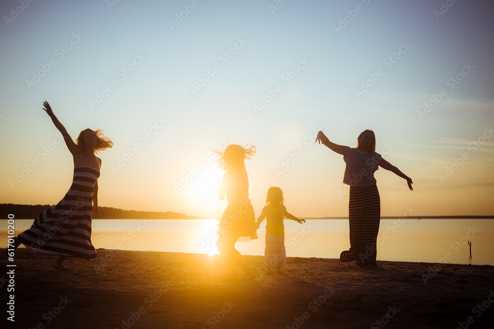 Fototapeta premium Silhouettes of group people dancing at sunset. Children and mothers jumping and having fun on the beach. Good mood. Active family pastime. Generations. Beautiful landscape. Enjoyment atmosphere