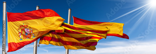 Close-up of Spanish and Catalan flags (la Rojigualda and Senyera) with flagpole, blowing in the wind on a blue sky with clouds, sunbeams and copy space. photo