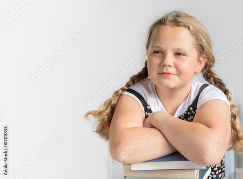 Portrait of a smiling teenage girl, a schoolgirl with two pigtails leaned on books on a light background with copy space