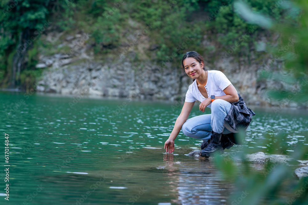 Fototapeta premium a young woman squats by the shore of the lake and enjoys the refreshing coolness and beauty of the lake