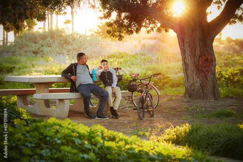 Father and son (12-13) relaxing in park after bike ride