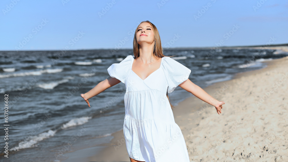 Happy smiling beautiful woman is on the ocean beach in a white summer dress, open arms Happy smiling beautiful woman is on the ocean beach in a white summer dress, open arms