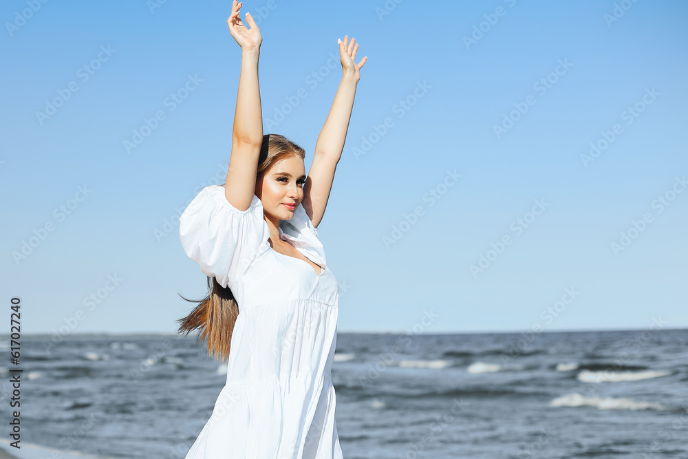 Happy smiling beautiful woman on the ocean beach standing in a white summer dress, raising hands Happy smiling beautiful woman on the ocean beach standing in a white summer dress, raising hands