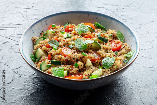 Quinoa tabbouleh salad in a bowl, a healthy dinner with tomatoes and mint on a black slate background