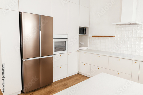 Modern minimal kitchen design. Modern kitchen interior. Stylish white kitchen cabinets with brass knobs, granite island and appliances in new scandinavian house.