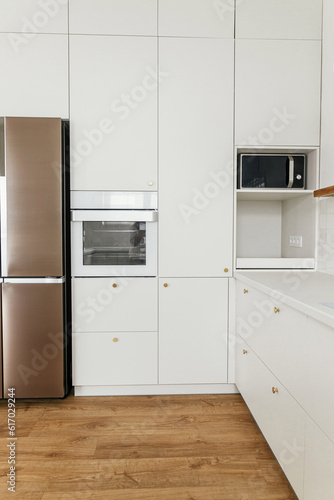 Modern minimal kitchen design. Stylish white kitchen cabinets with brass knobs, wooden shelves and appliances in new scandinavian house.  Modern kitchen interior
