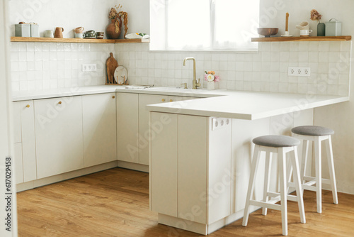 Modern kitchen interior. Stylish white kitchen cabinets with brass knobs, granite island, appliances and utensils on wooden shelves in new scandinavian house. Modern minimal kitchen design