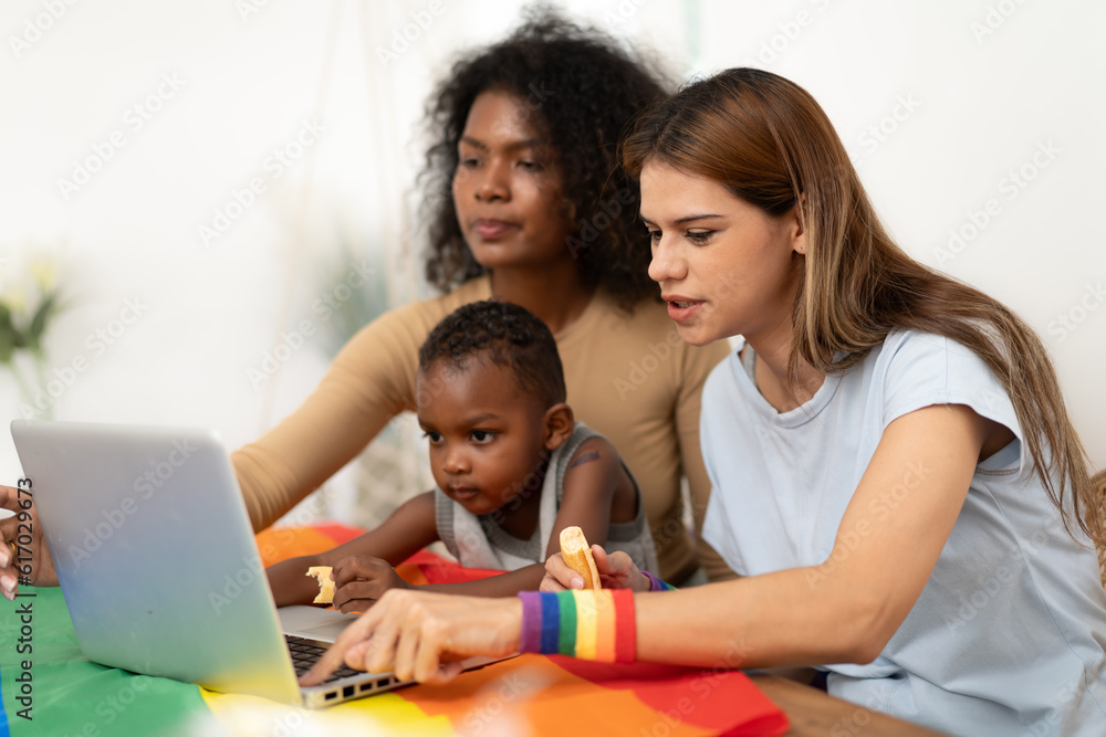 Happy multiethnic women couple having fun with her son watching movie at home. Lesbian mother and child study cyberspace using laptop. Happy female gay family. Homosexual, LGBT relationship lifestyle Happy multiethnic women couple having fun with her son watching movie at home. Lesbian mother and child study cyberspace using laptop. Happy female gay family. Homosexual, LGBT relationship lifestyle
