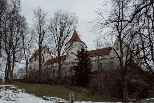 A small white castle in the old town of Füssen photographs in winter with light snow and a park in the foreground