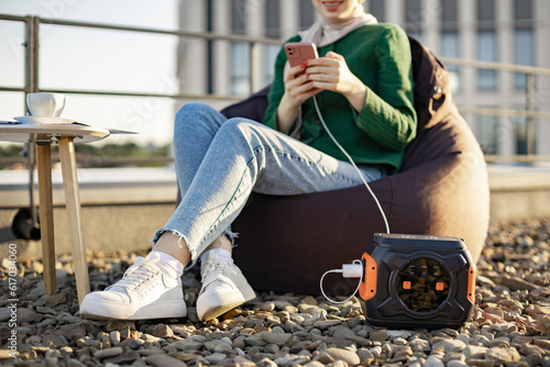 Cropped view of female in casual clothes getting access to internet over phone powered by portable charging station. Happy person staying in touch with friends outdoors due to energy storage system. photo