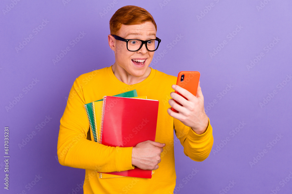 Portrait of smiling young college student with books use cellphone against violet color background Portrait of smiling young college student with books use cellphone against violet color background