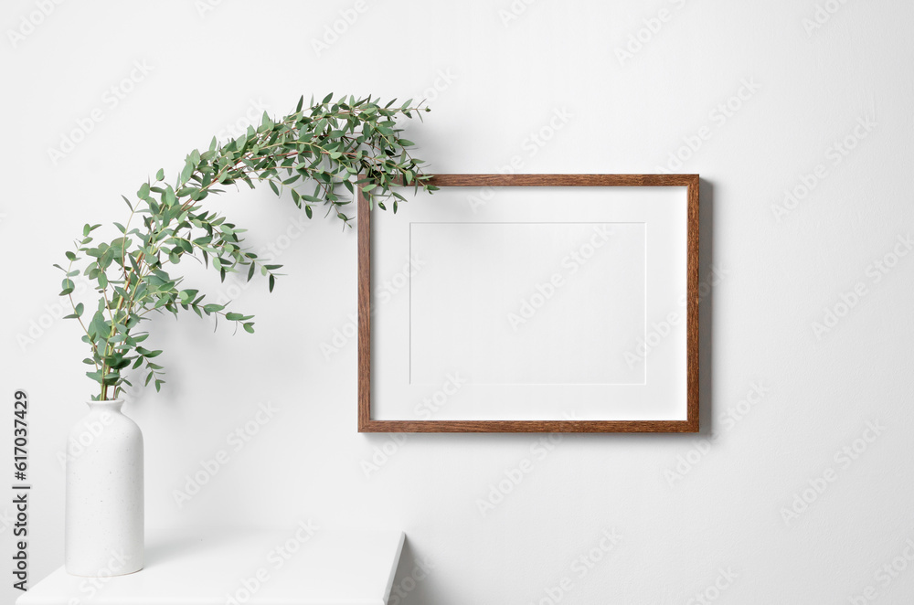 Blank landscape frame mockup for artwork on white wall with eucalyptus plant Blank landscape frame mockup for artwork on white wall with eucalyptus plant