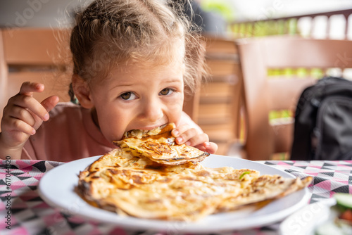 Little girl eating potato and cheese gozleme on wooden table. Traditional stuffed pancakes in Alanya  Turkey