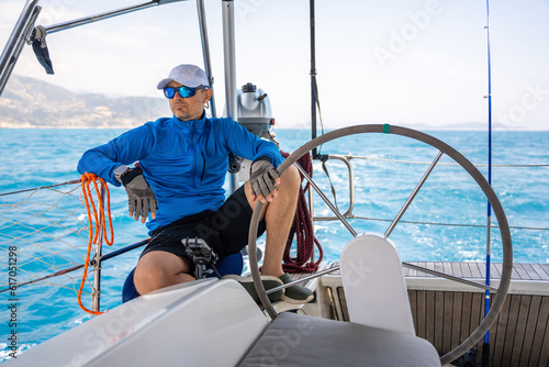 Young man captain stands at the helm and controls a sailboat during a journey by sea
