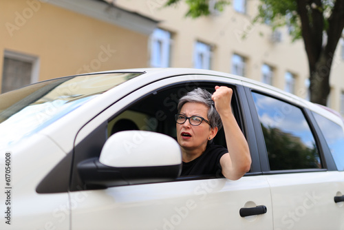 Female driver aggressively gesturing with her hand showing a fist. Stress and aggression concept among car drivers. © Andrii Zastrozhnov