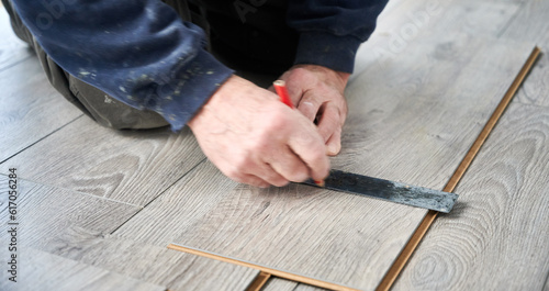 Close up of man hands using metal ruler and pencil while drawing line on laminate plank. Male construction worker measuring laminate wooden board for floor installation. Flooring renovation concept.
