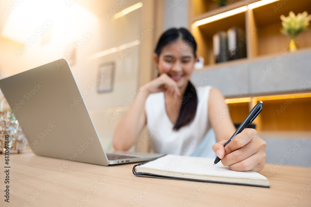 Asian female administrative assistant working and writing in notepad at home office. Woman planning working schedule Asian female administrative assistant working and writing in notepad at home office. Woman planning working schedule