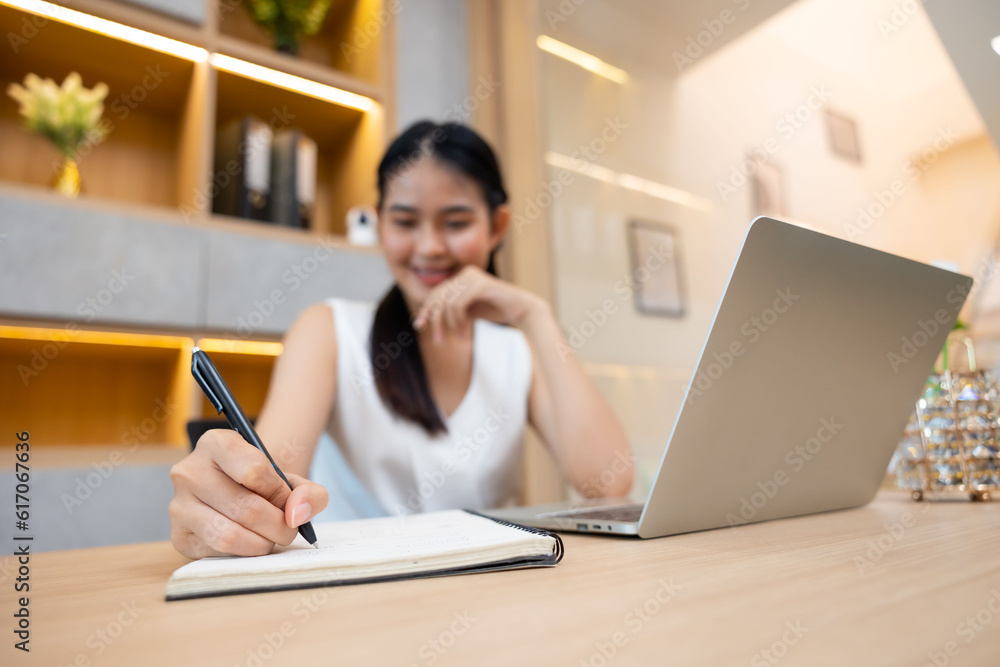 Asian female administrative assistant working and writing in notepad at home office. Woman planning working schedule Asian female administrative assistant working and writing in notepad at home office. Woman planning working schedule