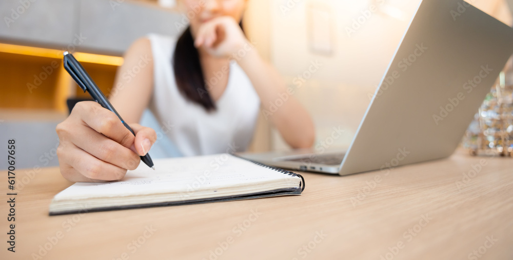 Asian female administrative assistant working and writing in notepad at home office. Woman planning working schedule Asian female administrative assistant working and writing in notepad at home office. Woman planning working schedule