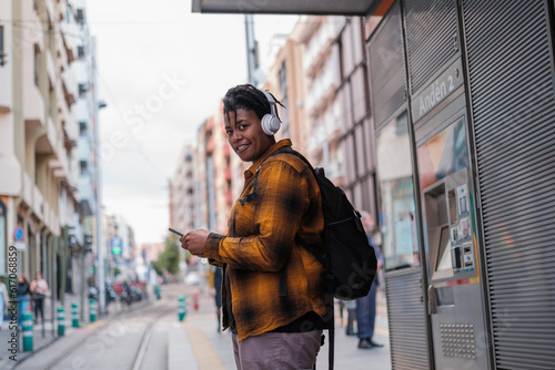 Young man in yellow checkered t-shirt using smartphone while waiting for the tram. Concept: public transport, lifestyle, urbanstyle