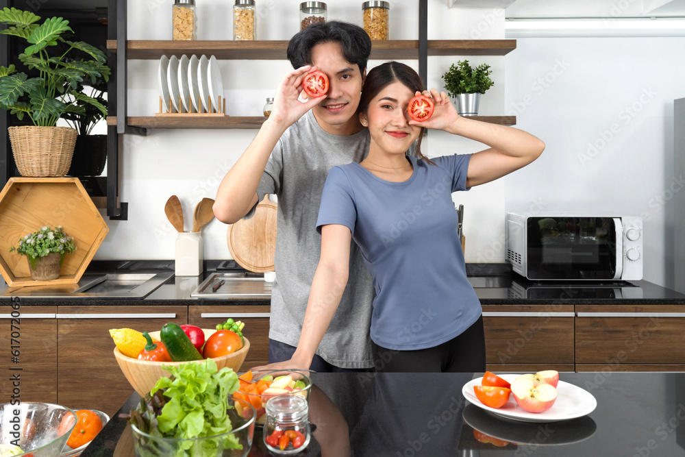 Young couple in casual clothe, hold slice tomato in eye position. Asian lover spend morning time together in the kitchen. Young couple in casual clothe, hold slice tomato in eye position. Asian lover spend morning time together in the kitchen.