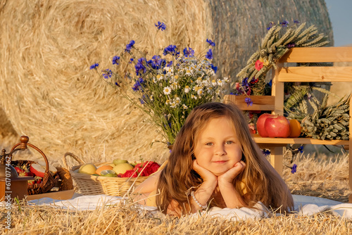 Cute girl lying in the field with her head propped up in her hands, around fruits and flowers, a picnic in retro style. amily summer fun in the country. Summer holidays. photo