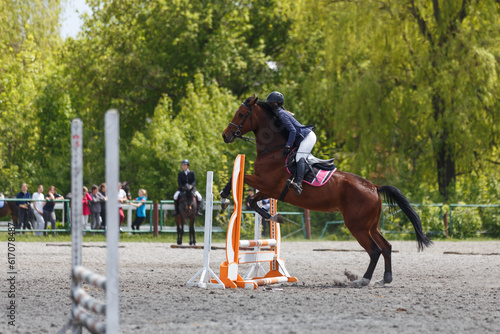 Young woman riding horseback jumping over the hurdle on showjumping course in equestrian sports event