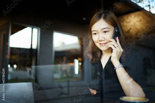 Happy cheerful Asian beautiful woman sitting in the coffee shop in front of the window and working on digital tablet and laptop - notebook computer.