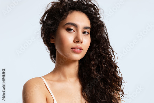 A girl with glowing skin and thick black and curly hair looks at the camera against a blue background