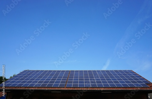 Großes Dach mit blauen Solarpanels von Haus vor blauem Himmel bei Sonne am Mittag im Sommer