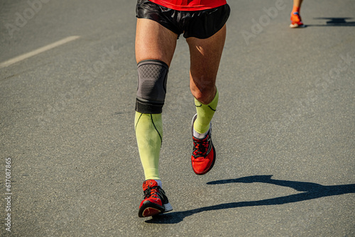 close-up legs male runner in compression socks and knee pads running marathon race, sports summer games photo