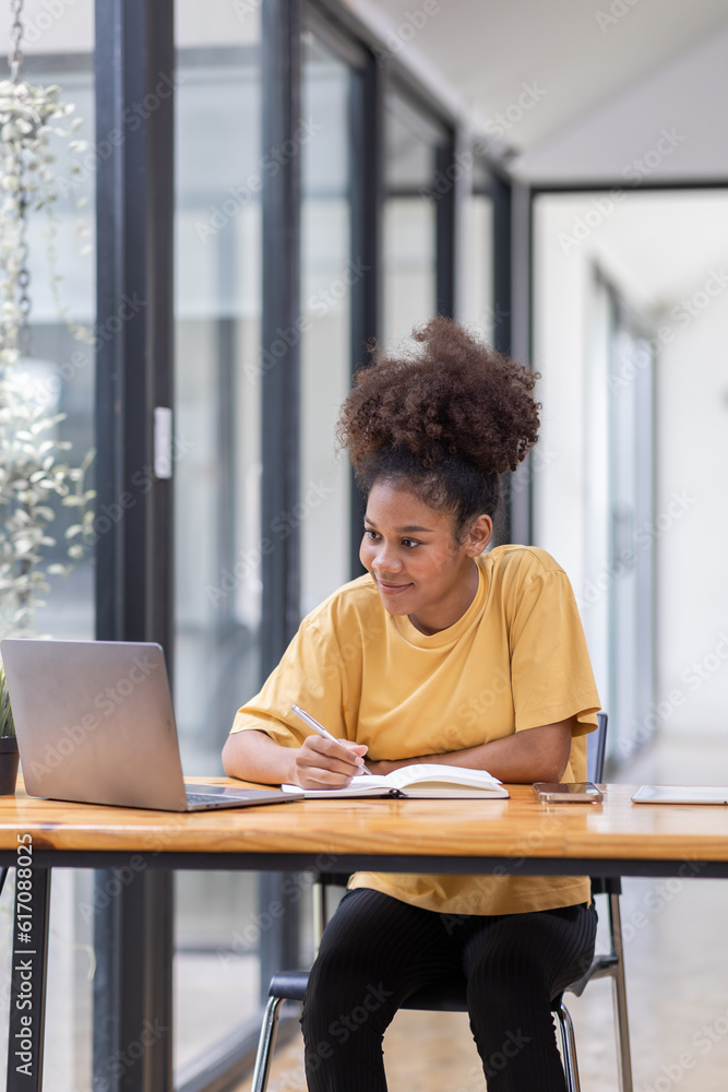 Business And Education Concept. Smiling african american sitting at desk working on laptop writing letter in paper documents, free copy space. Happy millennial female studying using laptop Business And Education Concept. Smiling african american sitting at desk working on laptop writing letter in paper documents, free copy space. Happy millennial female studying using laptop