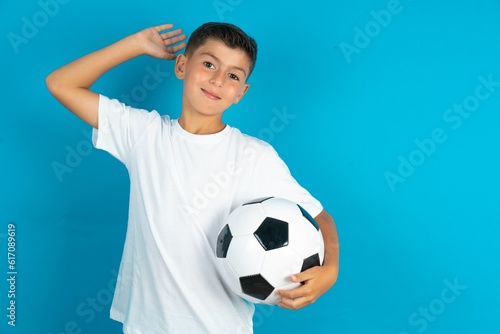 Little hispanic boy wearing white T-shirt holding a football ball stretching arms, relaxed position. © Jihan