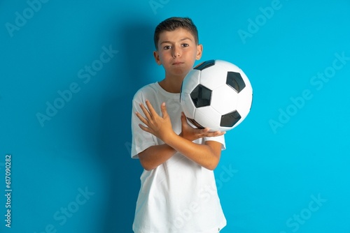 Little hispanic boy wearing white T-shirt holding a football ball Rejection expression crossing arms doing negative sign  angry face