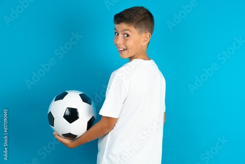 Satisfied pretty Little hispanic boy wearing white T-shirt holding a football ball beaming smile look camera © Jihan