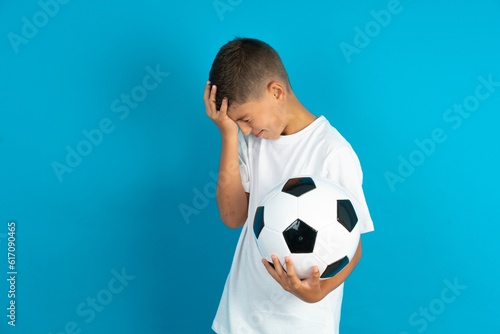 A very upset and lonely Little hispanic boy wearing white T-shirt holding a football ball crying 