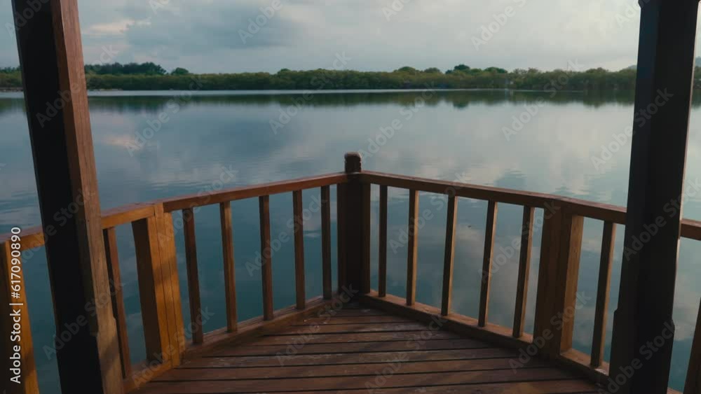 Beautiful static view of wooden gazebo on a tranquil lake in summer. Idyllic evening on terrace of house on a pond in middle of woods. Forest and reflection of sky on cal water. Sunset in countryside Beautiful static view of wooden gazebo on a tranquil lake in summer. Idyllic evening on terrace of house on a pond in middle of woods. Forest and reflection of sky on cal water. Sunset in countryside