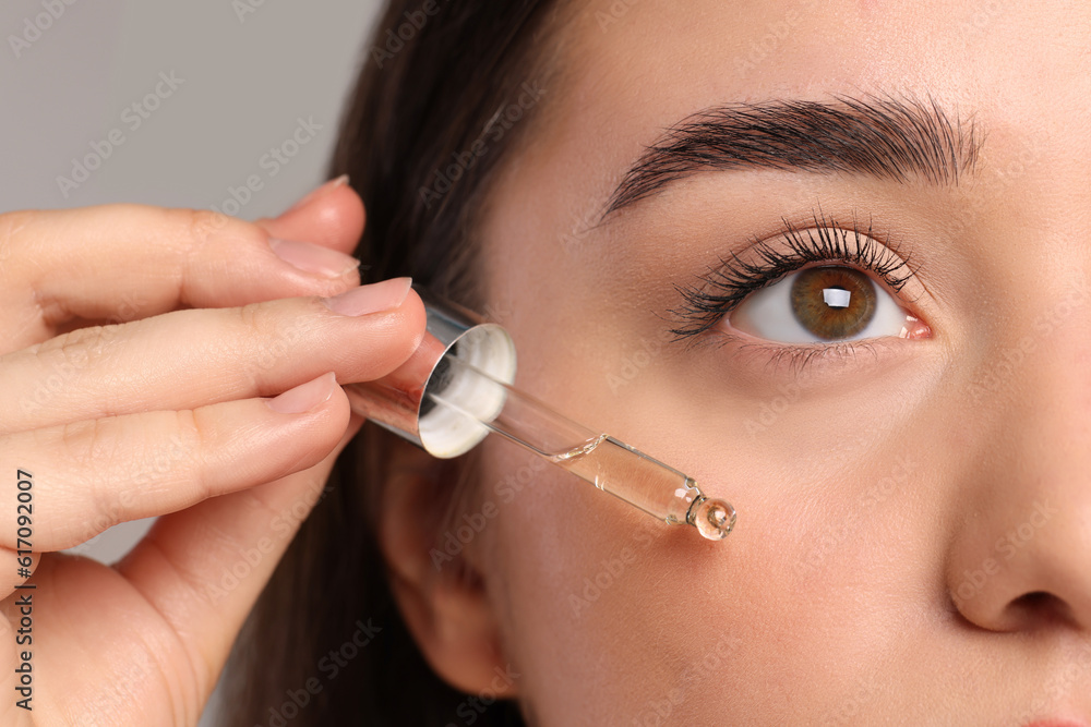 Young woman applying essential oil onto face on light grey background, closeup Young woman applying essential oil onto face on light grey background, closeup