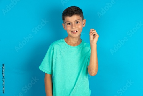 Little hispanic boy wearing green T-shirt pointing up with hand showing up seven fingers gesture in Chinese sign language QÄ«.