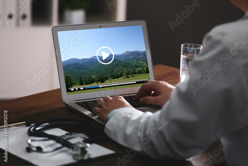 Doctor watching video on laptop at office desk, closeup. Man choosing vacation spots