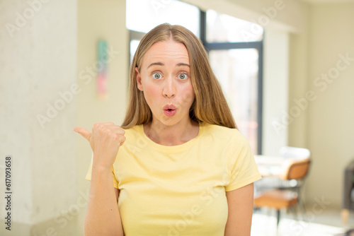 pretty blond woman looking astonished in disbelief, pointing at object on the side and saying wow, unbelievable